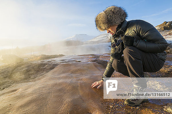 Frau berührt den Boden am Großen Geysir  einem Geysir  der im Haukadalur-Tal an den Hängen des Laugarfjall-Hügels im Südwesten Islands liegt