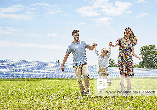Mutter und Vater halten mit dem Sohn Händchen und gehen über das Feld neben dem Solarpark