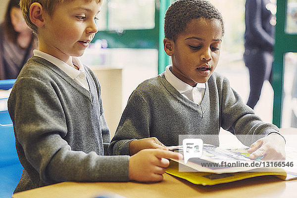 Zwei Jungen lesen ein Märchenbuch am Schreibtisch im Klassenzimmer der Grundschule