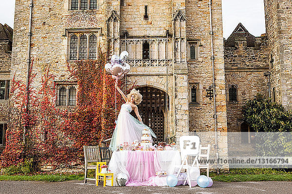 Bride standing on table outside castle  holding balloons