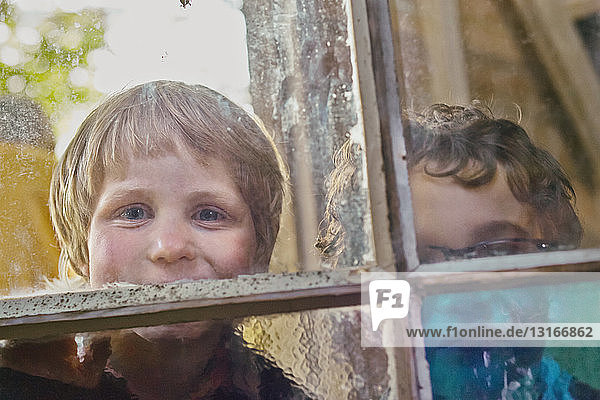 Porträt von zwei Jungen  die durch ein Hüttenfenster schauen