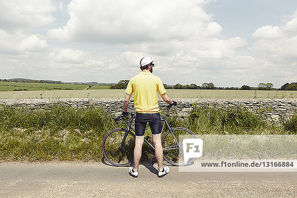 Cyclist standing by stone wall  Cotswolds  UK