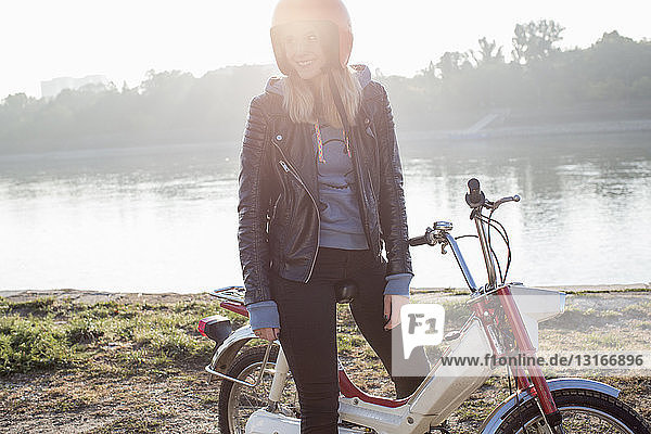 Junge Frau sitzt auf einem Retro-Moped am See