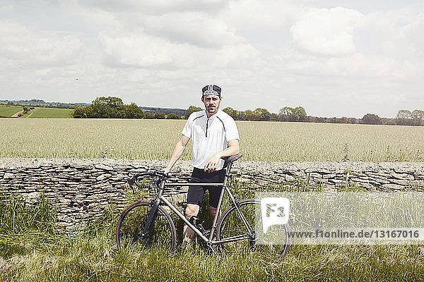 Cyclist standing by stone wall  Cotswolds  UK