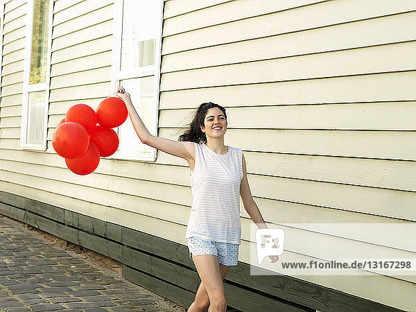 Junge Frau geht mit einem Haufen Luftballons durch eine Gasse