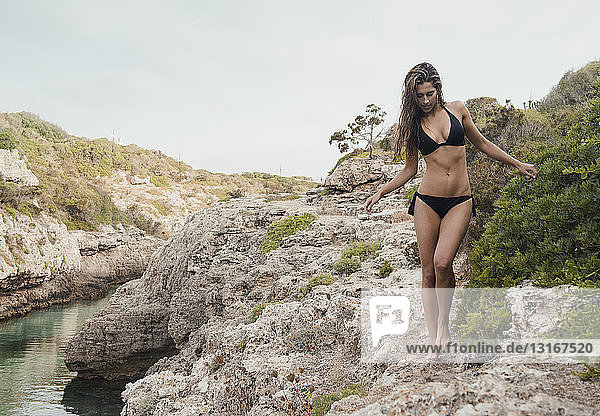 Young woman wearing bikini walking on rocks at Cala en Brut  Menorca  Balearic islands  Spain
