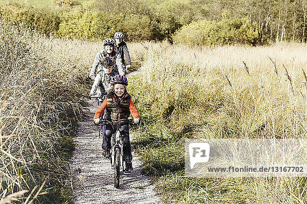 Frontansicht einer Familie  die auf einem ländlichen Weg mit dem Fahrrad unterwegs ist und lächelnd in die Kamera schaut