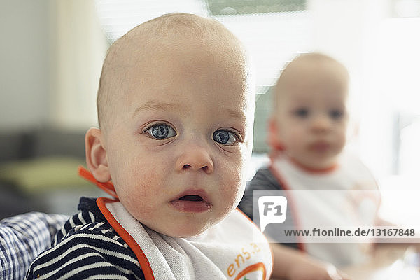 Portrait of staring baby twin brothers in high chairs