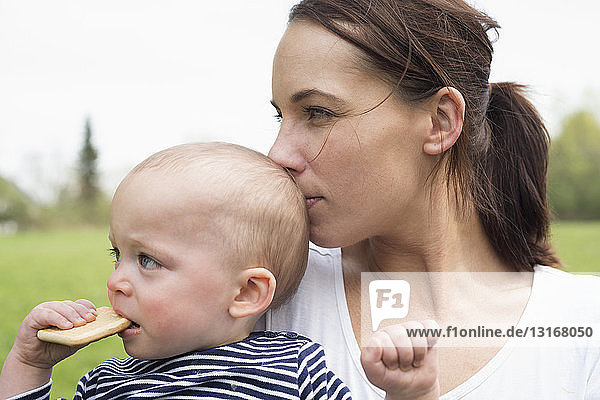 Portrait of young mother kissing baby son in field
