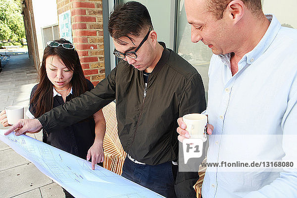 Drei Architektenkollegen inspizieren den Entwurf vor dem Büro
