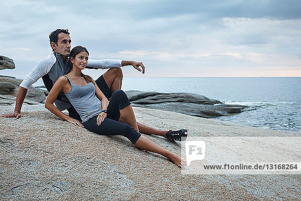 Ehepaar entspannt sich auf einem Felsblock am Meer