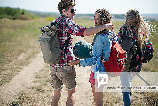 Three friends walking on dirt track with backpacks