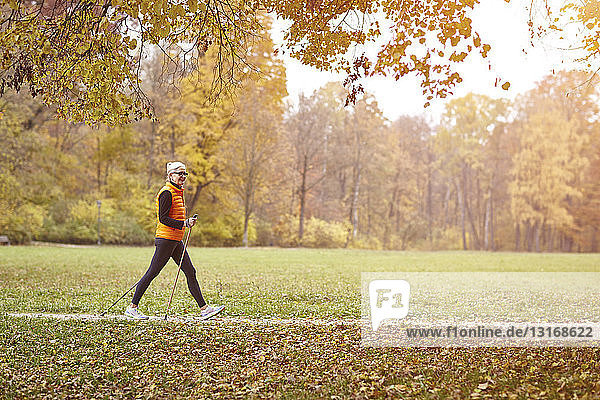 Senior female nordic walker walking on autumn park path