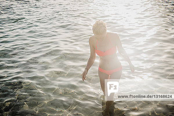 Mittelgroße erwachsene Frau im Bikini  die im sonnenbeschienenen Meer paddelt