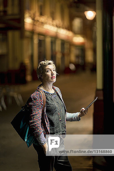 Portrait of mature woman using digital tablet on the street at night  London  UK