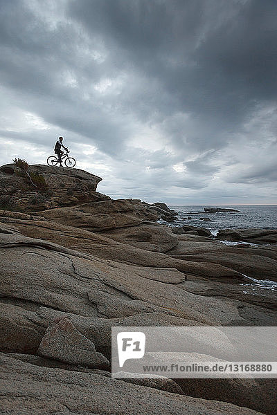 Mann sitzt auf Fahrrad auf Felsbrocken