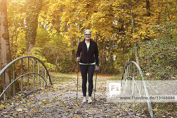 Senior female nordic walker crossing over footbridge in autumn park
