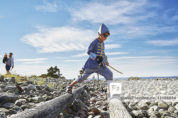 Als Pirat verkleideter Junge tritt am Strand über Holzscheite  Eggegrund  Schweden
