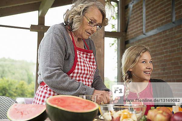 Mädchen und Großmutter am Küchentisch lernen  frisches Obst zu schneiden