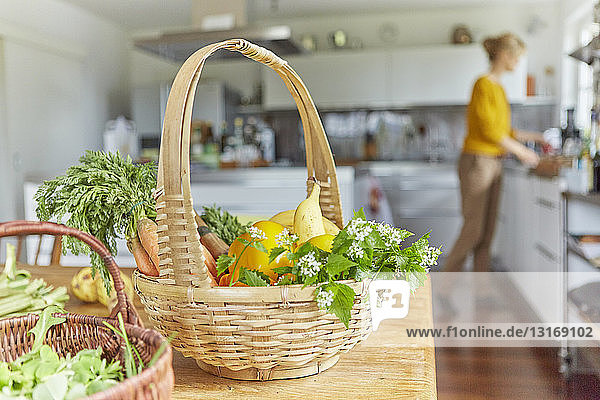 Gartenprodukte  in Körben auf dem Tisch in der Küche  reife Frau arbeitet im Hintergrund