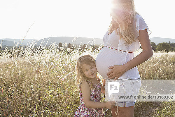 Mädchen hört Müttern mit schwangerem Bauch auf dem Feld zu