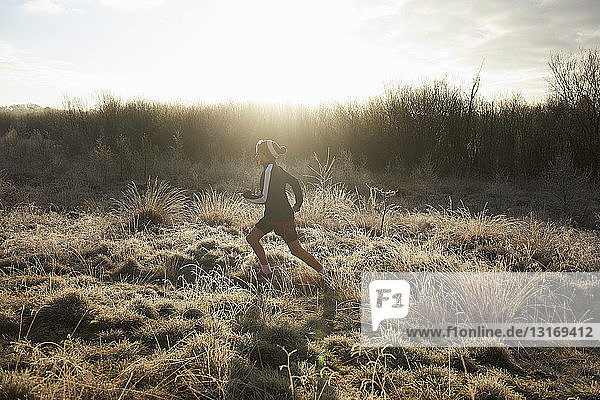 Side view of teenage boy running on frosty grassland