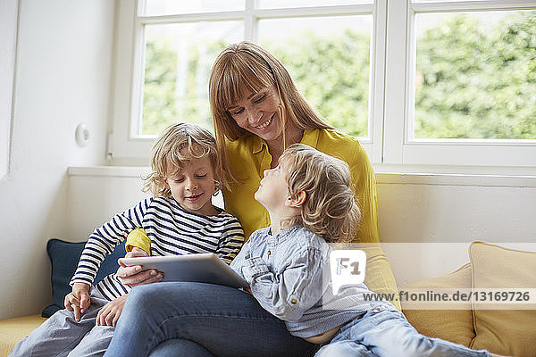 Mutter und zwei Söhne sitzen auf einem Fensterplatz und schauen auf ein digitales Tablett