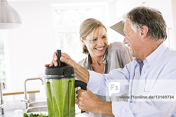 Couple preparing green vegetable smoothie in kitchen