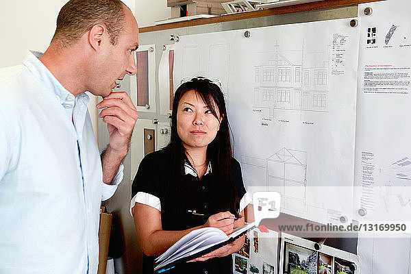 Male and female architects looking at blueprints in office