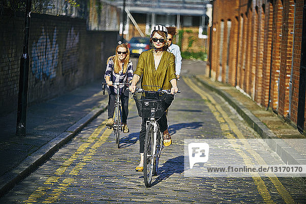 Frontansicht von Frauen mit Sonnenbrille beim Fahrradfahren auf Kopfsteinpflaster