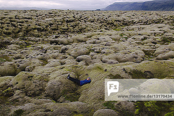 Seitenansicht einer mittleren erwachsenen Frau  die auf einer hügeligen Vulkanlandschaft liegt  Island