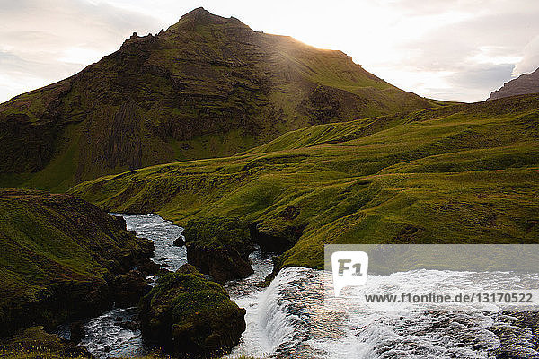 Fluss fließt durch eine üppig grüne Bergkette  Island