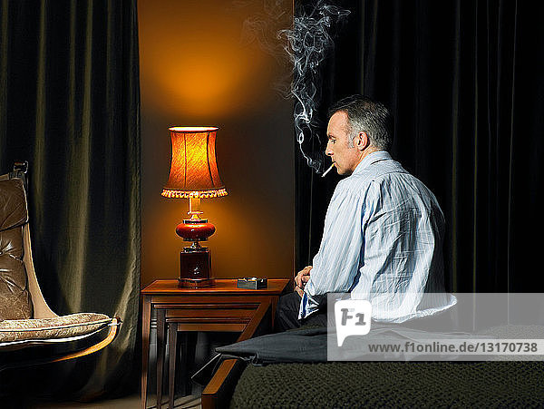 Man sitting on bed smoking a cigarette