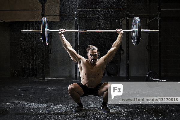 Junger Mann mit nackter Brust beim Gewichtheben in dunkler Turnhalle
