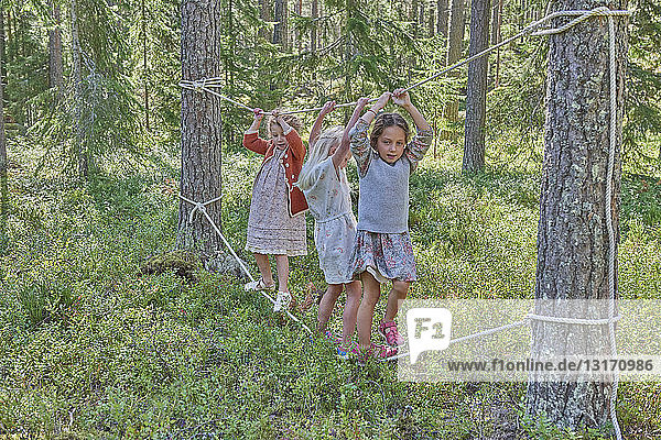 Girls wearing retro clothes balancing on ropes in forest