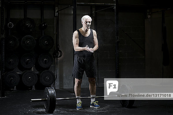 Älterer Mann kreidet Hände zum Gewichtheben in dunkler Turnhalle