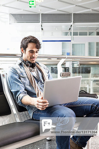 Mann mit Laptop im Wartebereich des Flughafens