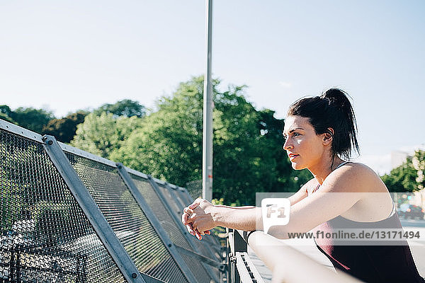 Seitenansicht einer erschöpften Sportlerin  die sich an der Brücke auf ein Geländer stützt
