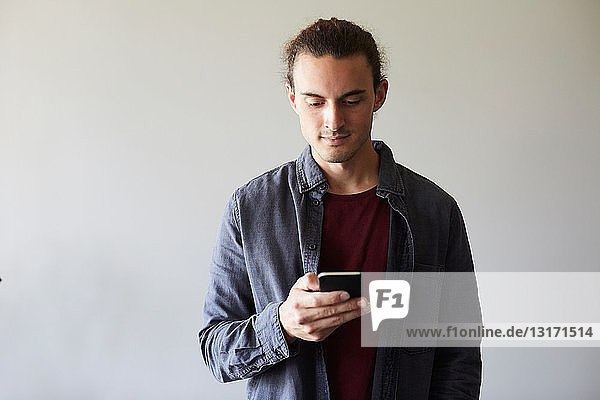 Creative businessman using mobile phone against gray wall in office