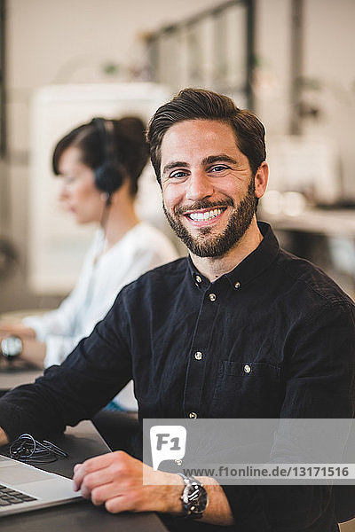 Portrait of smiling businessman sitting at desk in creative office