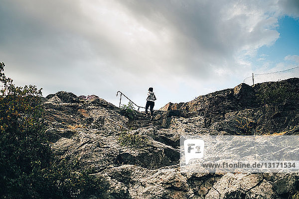 Niedrigwinkelansicht einer Athletin  die auf einem Hügel auf Felsen klettert  gegen den Himmel