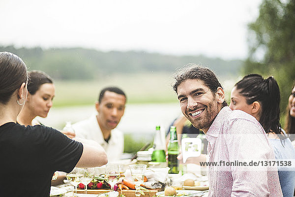 Portrait of smiling young man enjoying dinner with friends at table in backyard