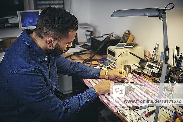 Männlicher Ingenieur beim Reparieren von Mobiltelefonen am Tisch in der Werkstatt