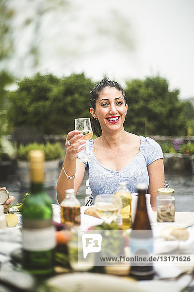 Lächelnde junge Frau schaut weg  während sie bei einer Dinnerparty Wein genießt