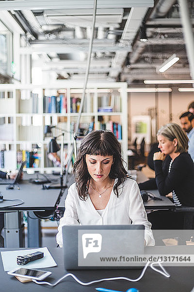 Female entrepreneur using laptop at desk in creative office