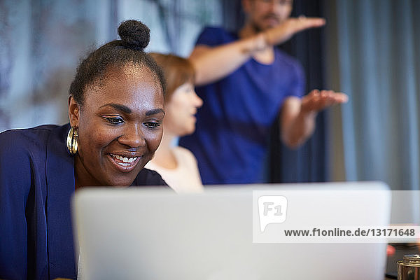 Kreative Geschäftsfrau lächelt  während sie bei einer Besprechung mit Kollegen im Büro den Laptop benutzt