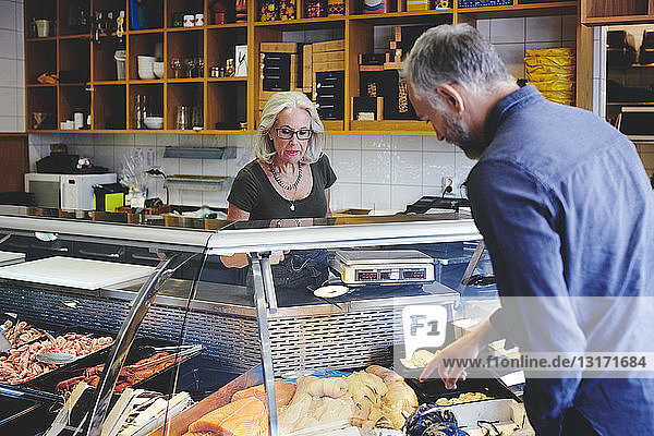 Kunde zeigt einer Verkäuferin im Feinkostladen Meeresfrüchte im Einzelhandel
