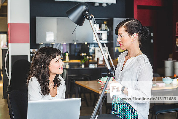 Businesswoman listening to female colleague at desk in creative office