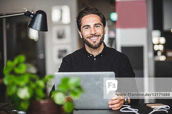Portrait of confident businessman sitting at desk in creative office