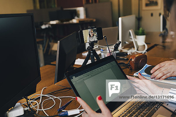Beschnittenes Bild eines reifen Computerprogrammierers  der einen Laptop und ein Smartphone im Büro benutzt